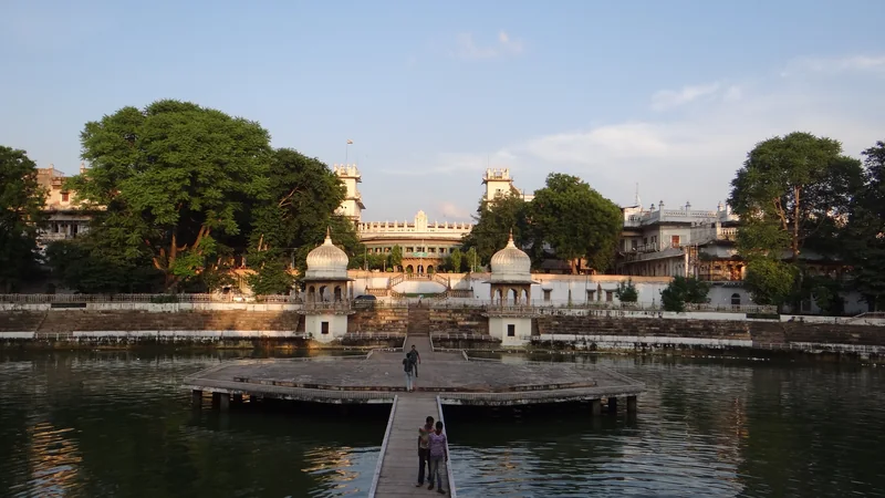 बैजाताल के पानी के बीच गोल मंच तक जाता संकरा रास्ता, किनारों पर सीढ़ियाँ और छतरियाँ, पीछे मोती महल।