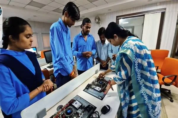 टेबल पर खुले इलेक्ट्रॉनिक उपकरण के पास नीली वर्दी में छात्र और एक प्रशिक्षक